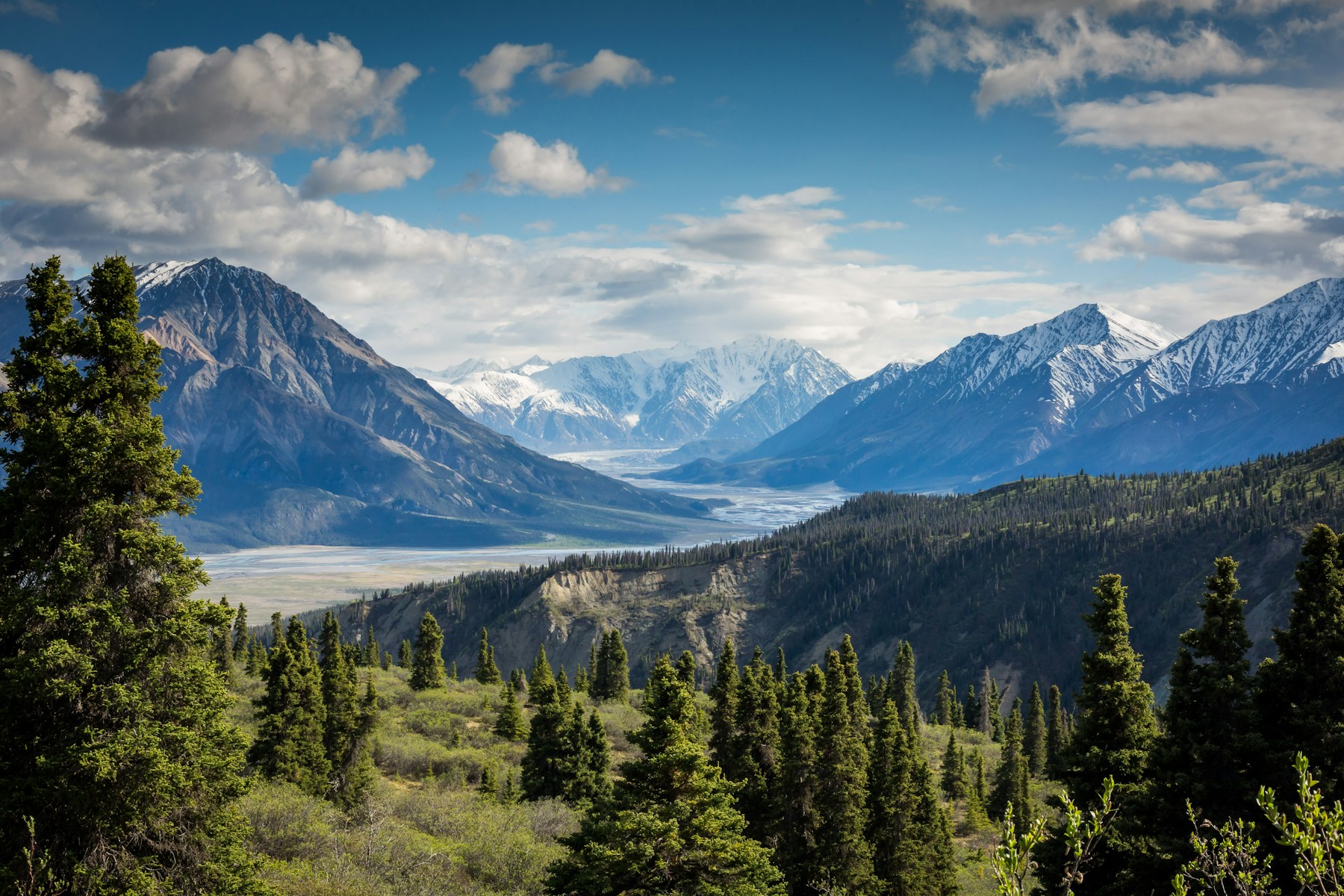 Sunlight over an alpine valley, with forested slopes and distant mountains